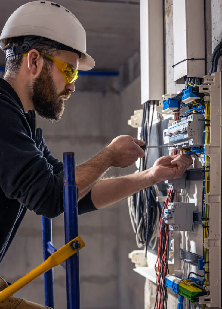 A skilled male electrician from Advanced Training Institute carefully connects electrical cables to a switchboard, ensuring safe and reliable power distribution.