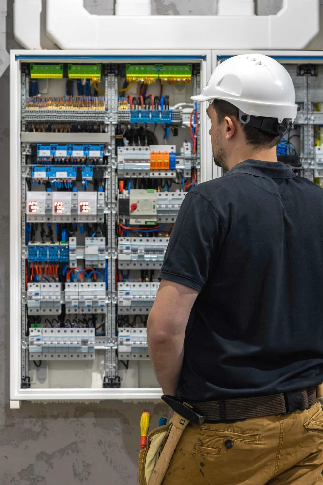 A skilled male electrical technician from Advanced Training Institute carefully inspects and maintains a switchboard equipped with fuses, ensuring safe and reliable power distribution